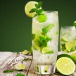 green apple mojito in glass with ice cubes, lemon slices and mint leaves.