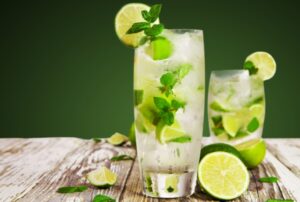 green apple mojito in glass with ice cubes, lemon slices and mint leaves.