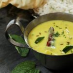 kadhi in the bowl which is beside plate of rice.