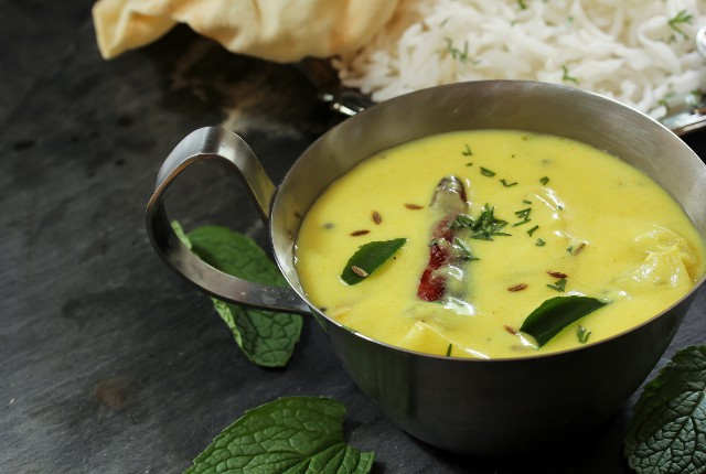 kadhi in the bowl which is beside plate of rice.