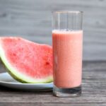 watermelon milkshake in glass and beside the glass watermelon slice in white color plate.