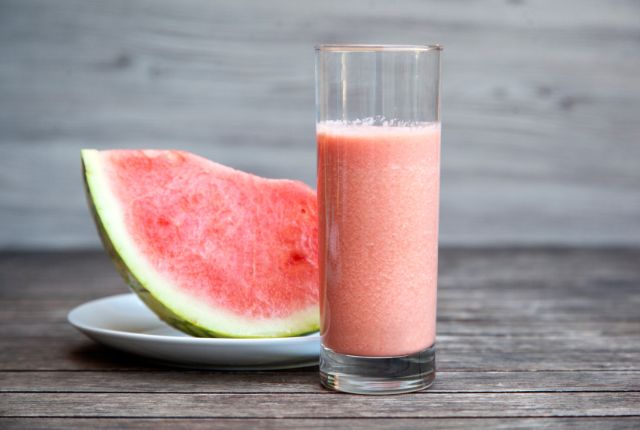 watermelon milkshake in glass and beside the glass watermelon slice in white color plate.
