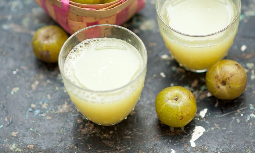 amla juice in the glass, beside the glass amla on the surface.