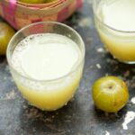 amla juice in the glass, beside the glass amla on the surface.