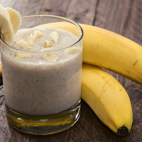 korean banana milk in glass with banana slice. Beside the glass 2 pieces of banana on the surface.