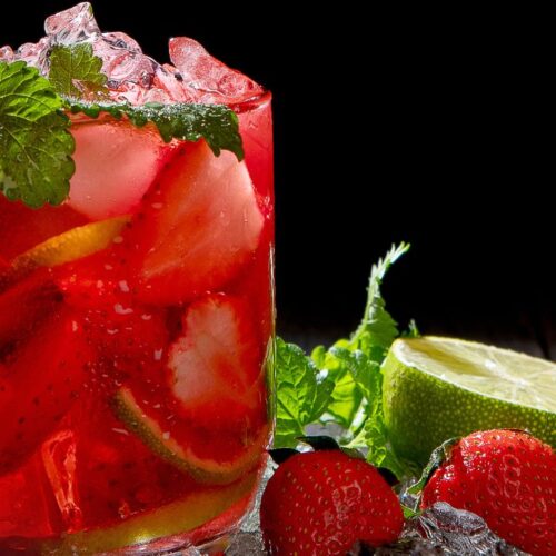 strawberry mojito in glass with mint leaves, ice cubes and strawberry pieces.
