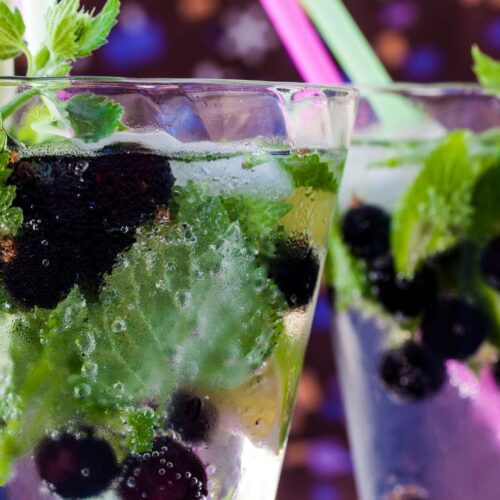 Blackcurrant mojito in glass with mint leaves, straw and lemon slice.