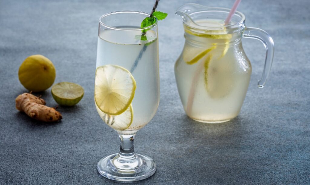 shikanji in wine glass with lemon slice and mint leaves. beside the glass lemon, ginger and jar on the surface.