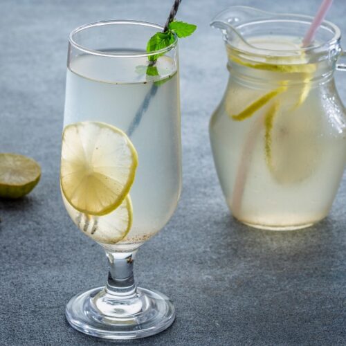 shikanji in wine glass with lemon slice and mint leaves. beside the glass lemon, ginger and jar on the surface.