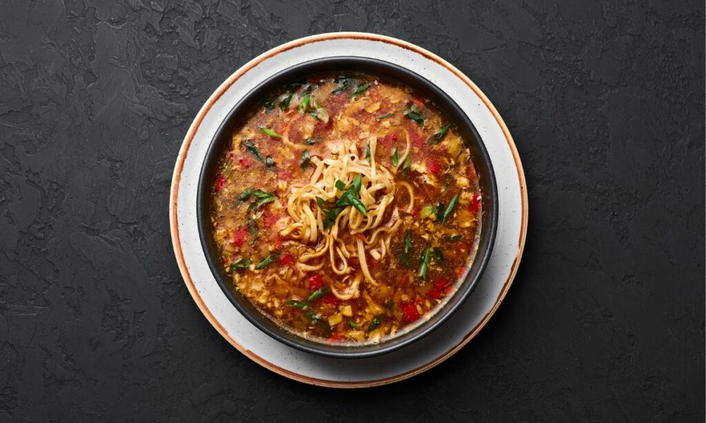 veg talumein soup in black color bowl.