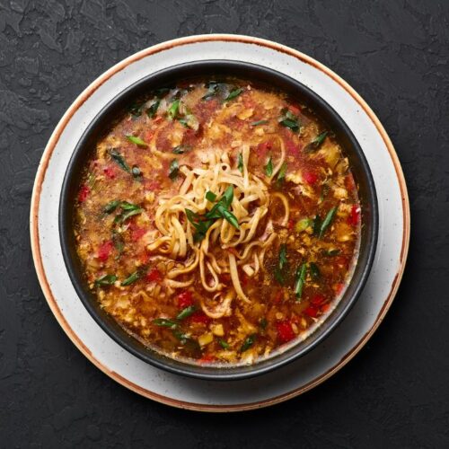 veg talumein soup in black color bowl.