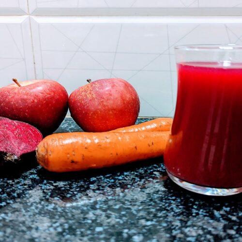 abc juice in glass, beside apples, beetroot, and carrot on the kitchen benchtops.