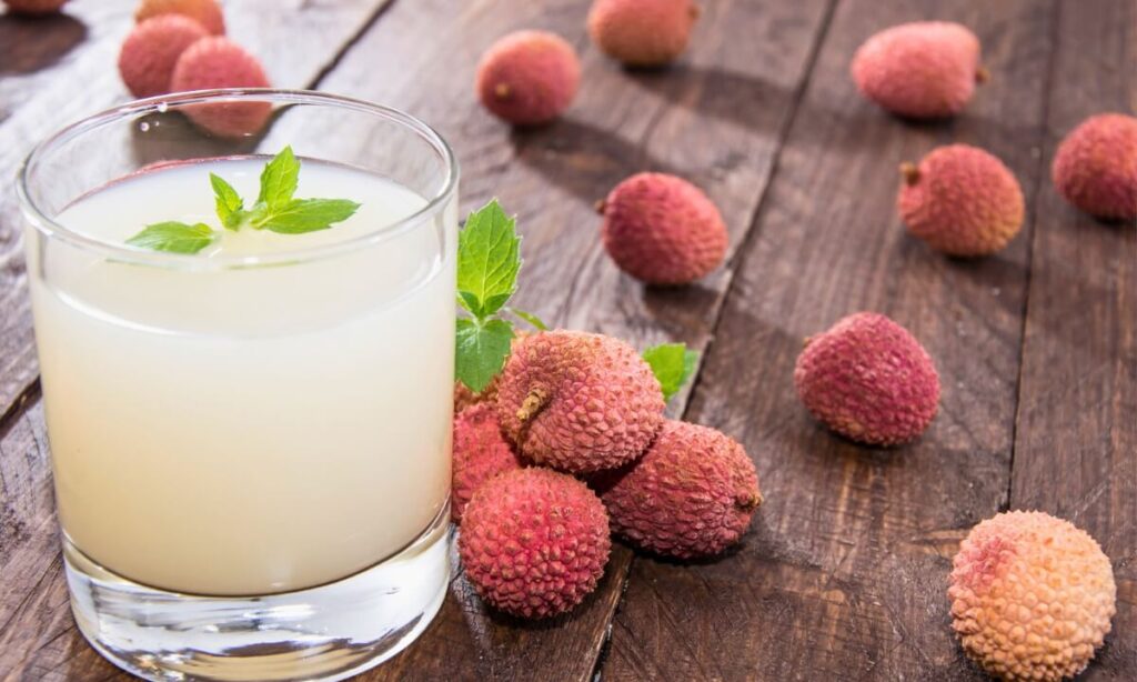 A glass of lychee juice next to lychee fruits.