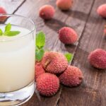 A glass of lychee juice next to lychee fruits.